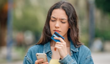 woman checking her phone with debit card and a concerned face 