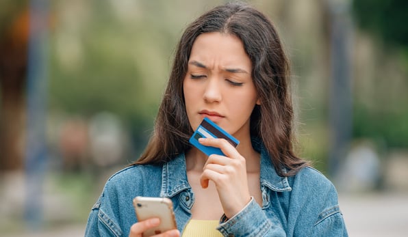 woman checking her phone with debit card and a concerned face 